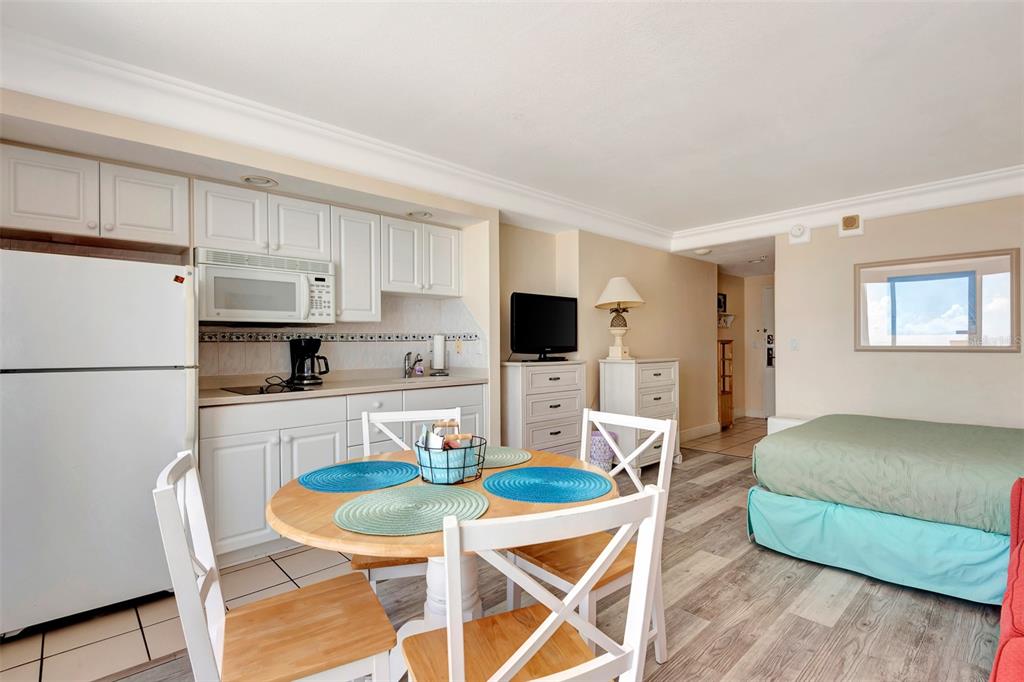 A studio apartment features a kitchen with white cabinets, a dining table, and a bed — 2700 N ATLANTIC AVENUE UNIT 1006, DAYTONA BEACH, FL