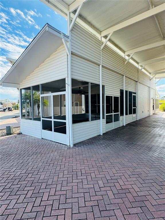 A screened-in porch with white siding sits under a large metal carport on brick pavers — 1144 DEER CREEK BOULEVARD, DAVENPORT, FL