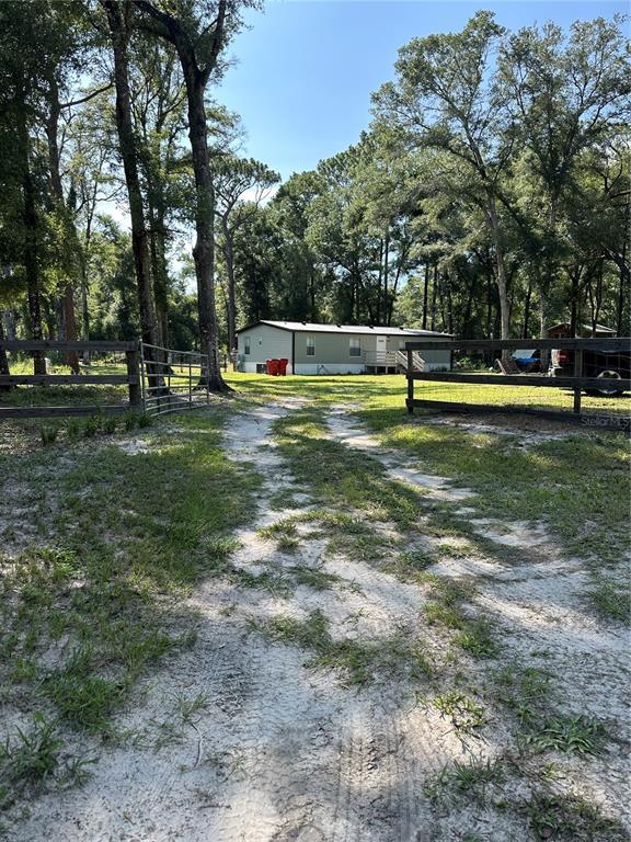 A single-story manufactured home sits at the end of a sandy driveway behind wooden fencing — 11882 SW 58TH STREET, WEBSTER, FL