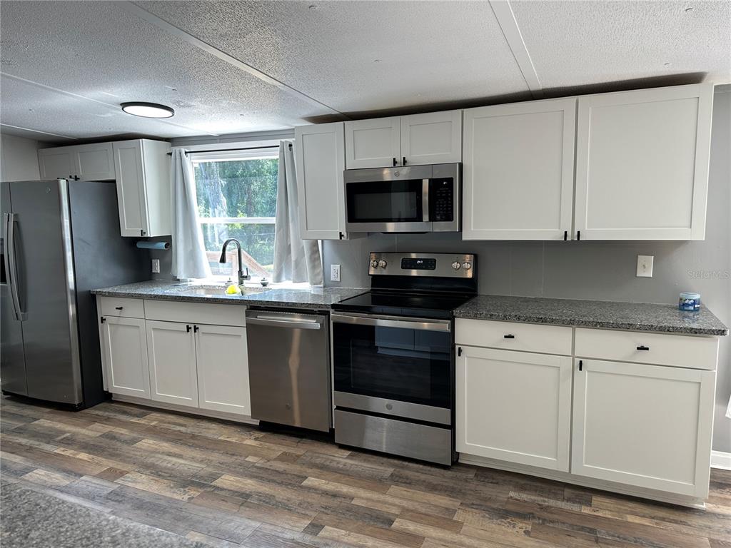 A kitchen features white cabinets, stainless steel appliances, granite countertops, and wood-look flooring — 11882 SW 58TH STREET, WEBSTER, FL