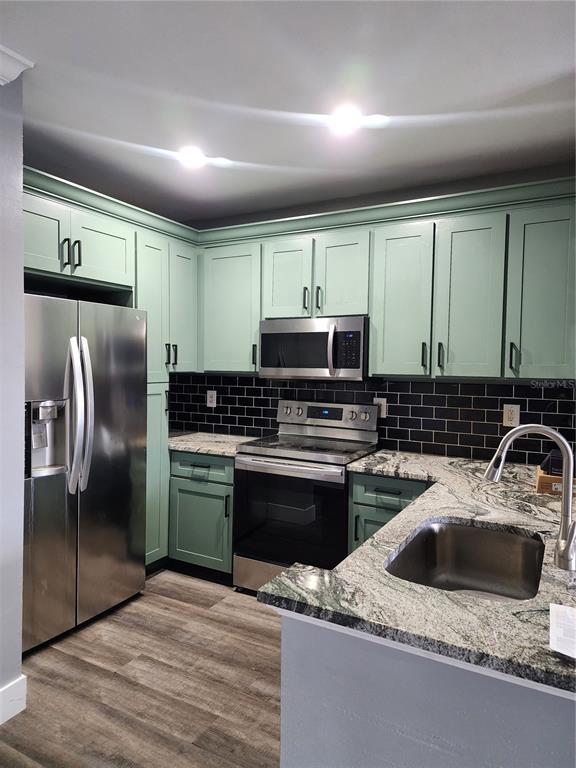 A kitchen features light green cabinets, black subway tile backsplash, granite countertops, and stainless appliances — 206 E SOUTH STREET UNIT 6034, ORLANDO, FL