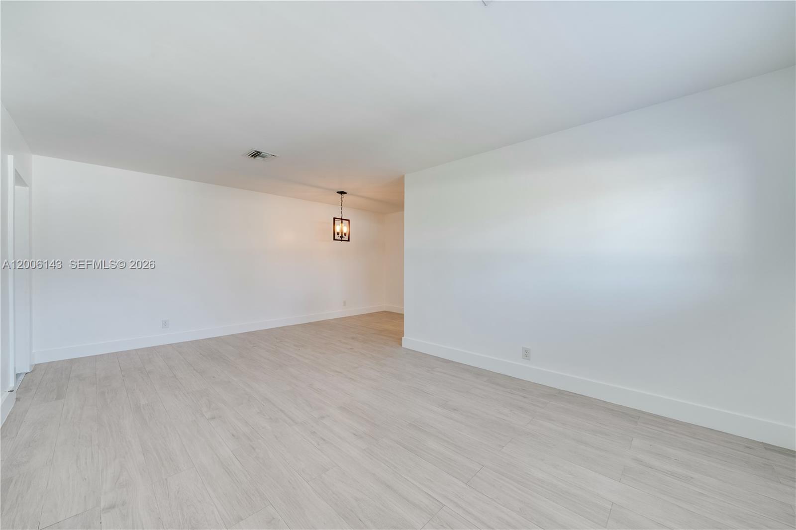 An empty room features white walls, light wood-look flooring, and a hanging pendant light — 8048 SW 80 AVE # 8048, Miami FL 33143, MIAMI, FL
