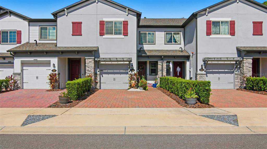 A row of three attached townhomes with brick driveways, gray siding, and red window shutters — 212 EVERTREE LOOP, SANFORD, FL
