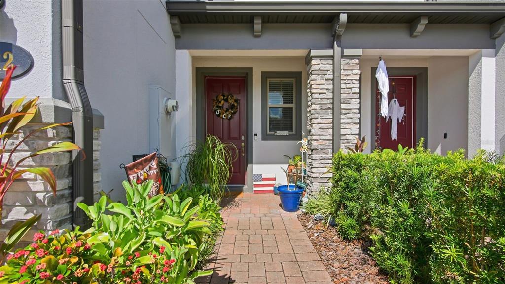A brick walkway leads to two red front doors with stone-accented pillars and landscaping — 212 EVERTREE LOOP, SANFORD, FL