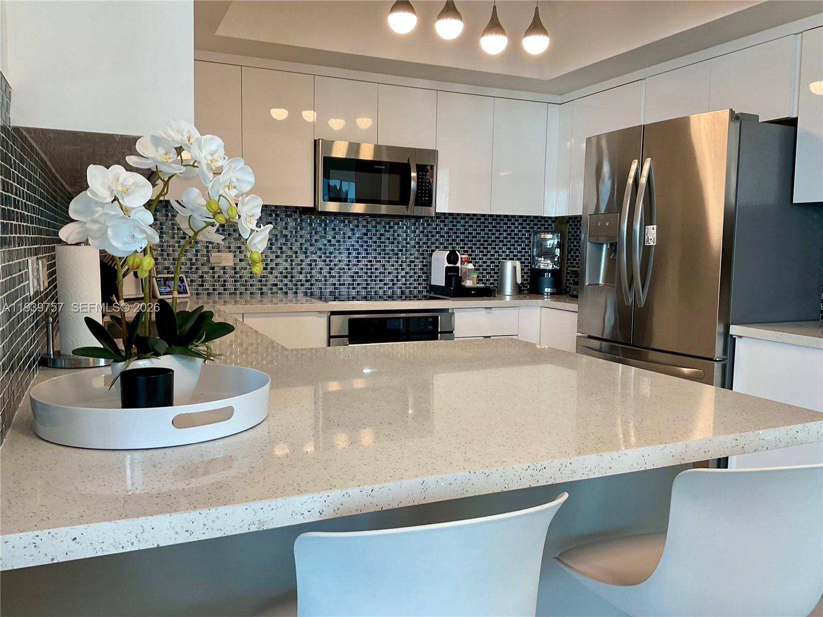 A modern kitchen features white cabinets, stainless steel appliances, and a speckled quartz countertop island — 140 S Dixie Hwy # 527, Hollywood FL 33020, HOLLYWOOD, FL