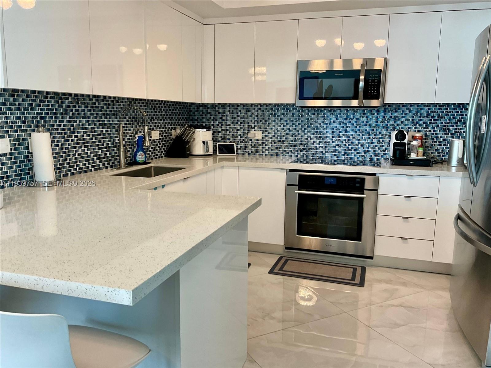 A modern kitchen features white cabinets, quartz countertops, and a blue glass tile backsplash — 140 S Dixie Hwy # 527, Hollywood FL 33020, HOLLYWOOD, FL