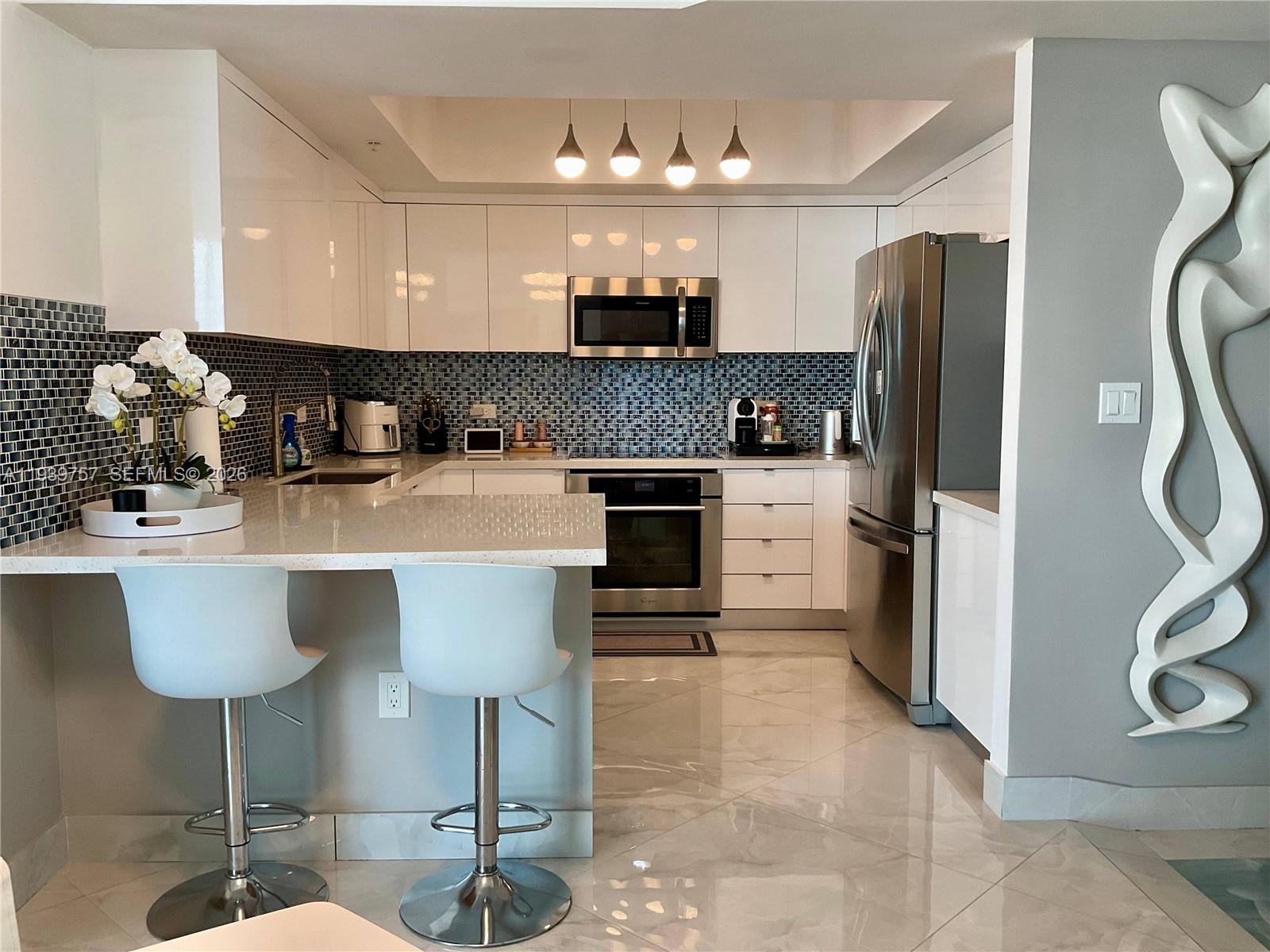A modern kitchen features white cabinets, stainless steel appliances, a mosaic backsplash, and a breakfast bar — 140 S Dixie Hwy # 527, Hollywood FL 33020, HOLLYWOOD, FL