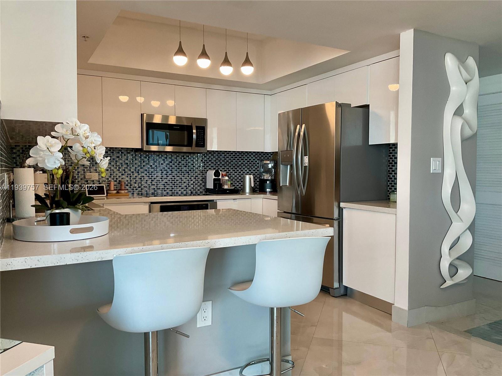 A modern kitchen features white cabinetry, stainless steel appliances, a tiled backsplash, and a breakfast bar — 140 S Dixie Hwy # 527, Hollywood FL 33020, HOLLYWOOD, FL