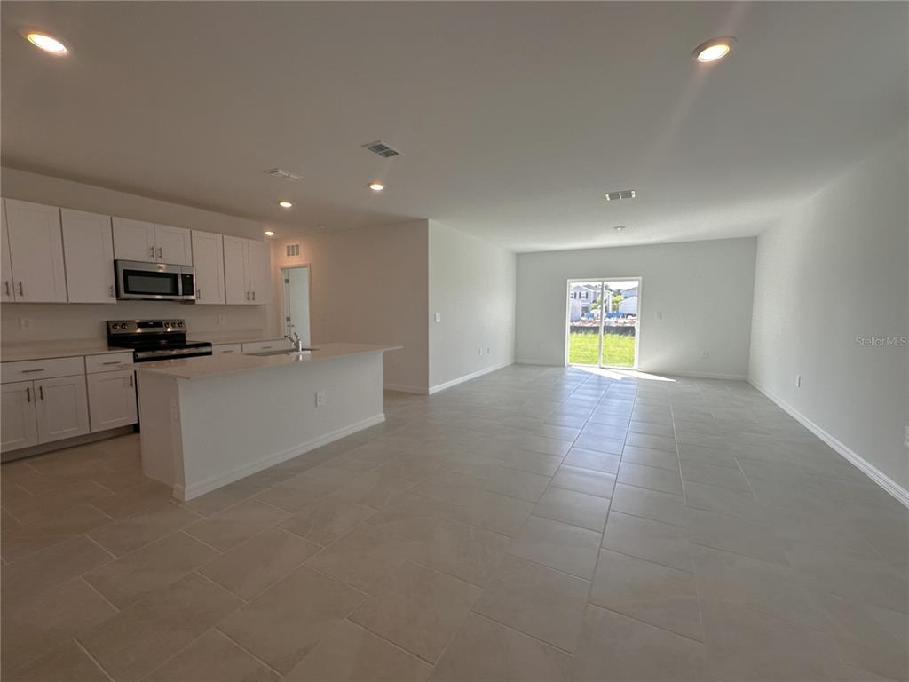 An open-concept kitchen with white cabinets and an island overlooks a spacious tiled living area — 11847 CLOVERLY LANE, PUNTA GORDA, FL
