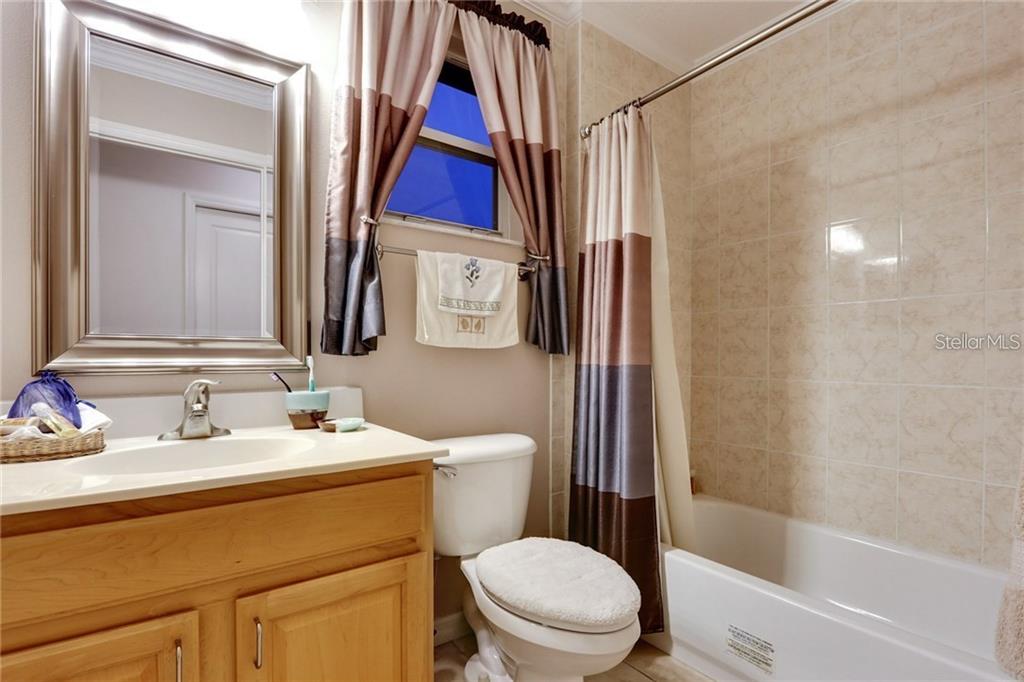 A bathroom features a wooden vanity, a toilet, and a shower-tub combination with tiled walls — 6020 CATLIN DRIVE, TAMPA, FL