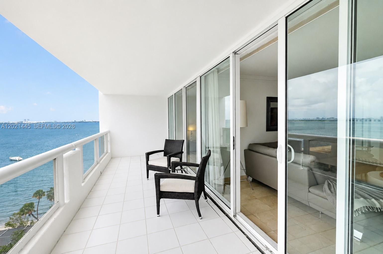 A balcony with white tile flooring features two chairs overlooking a large body of water — 1717 N Bayshore Dr # 1437, Miami FL 33132, MIAMI, FL