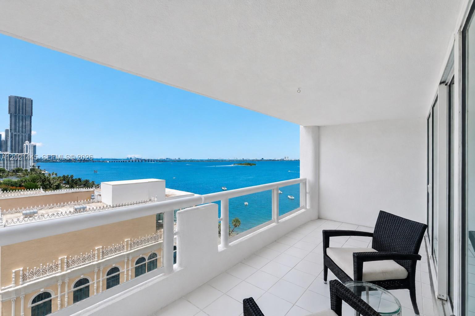 A balcony with white tile flooring, a glass railing, and two chairs overlooking the ocean — 1717 N Bayshore Dr # 1437, Miami FL 33132, MIAMI, FL