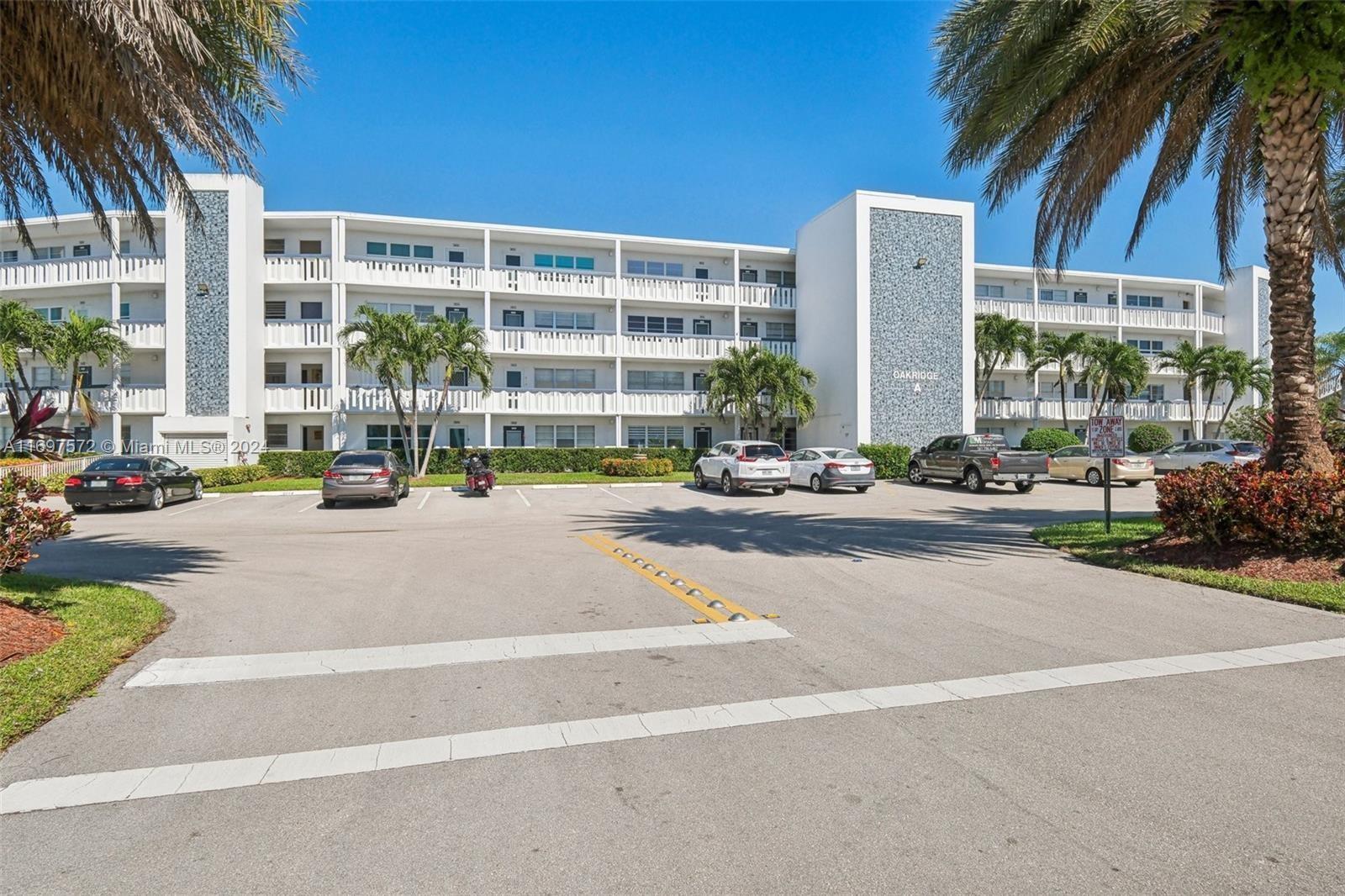 A multi-story white apartment building with a parking lot in front under a clear sky — 3014 Oakridge A # 3014, Deerfield Beach FL 33442, DEERFIELD BEACH, FL