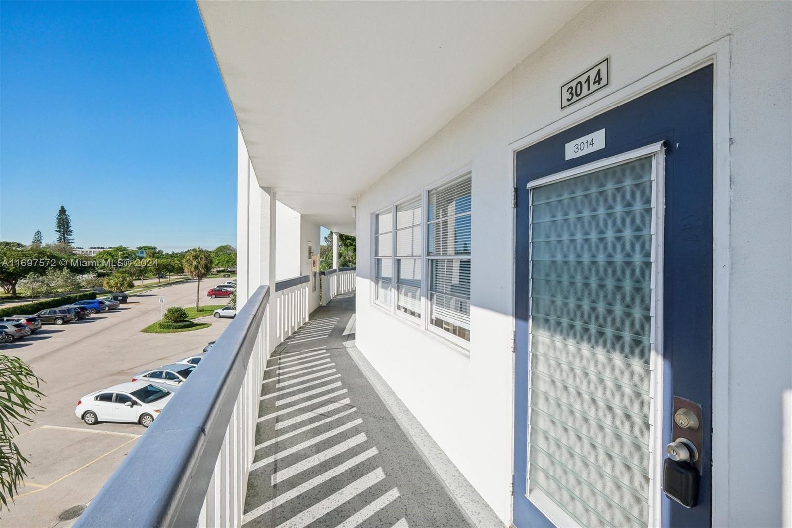 An exterior walkway features a blue door with a lockbox and a view of a parking lot — 3014 Oakridge A # 3014, Deerfield Beach FL 33442, DEERFIELD BEACH, FL