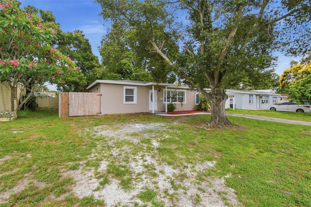 A single-story house with a beige exterior, a wooden fence, and a large front tree — 8331 55TH STREET N, PINELLAS PARK, FL