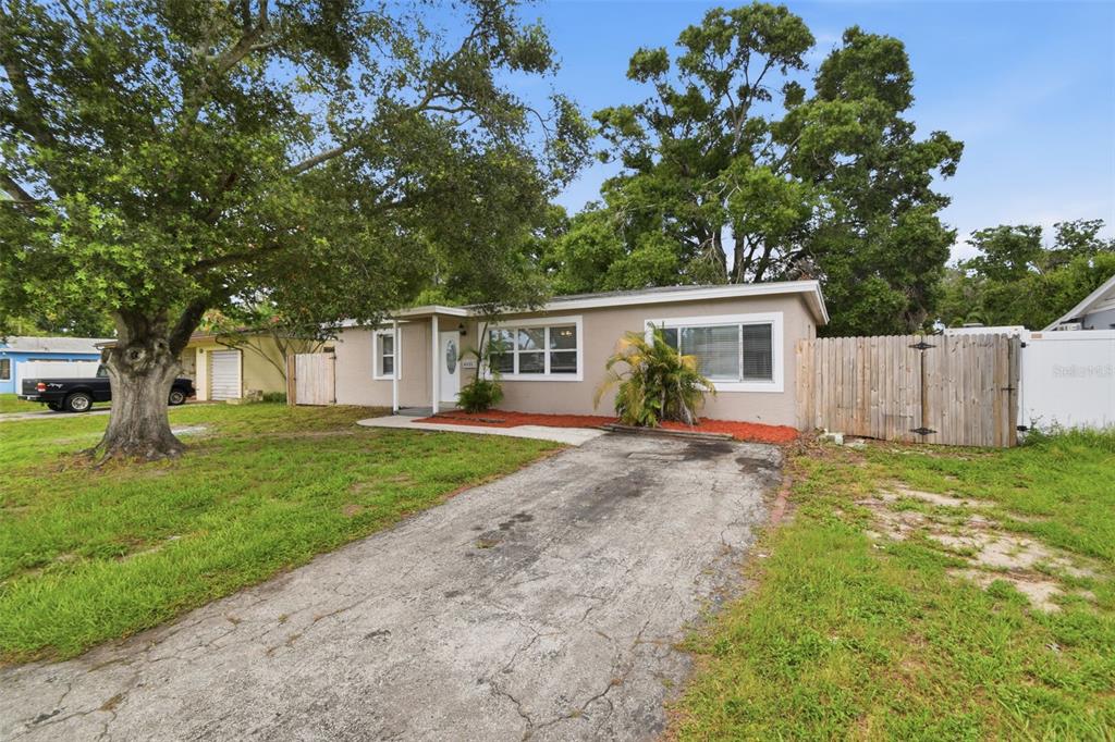 A single-story house with a beige exterior, a cracked concrete driveway, and large shade trees — 8331 55TH STREET N, PINELLAS PARK, FL