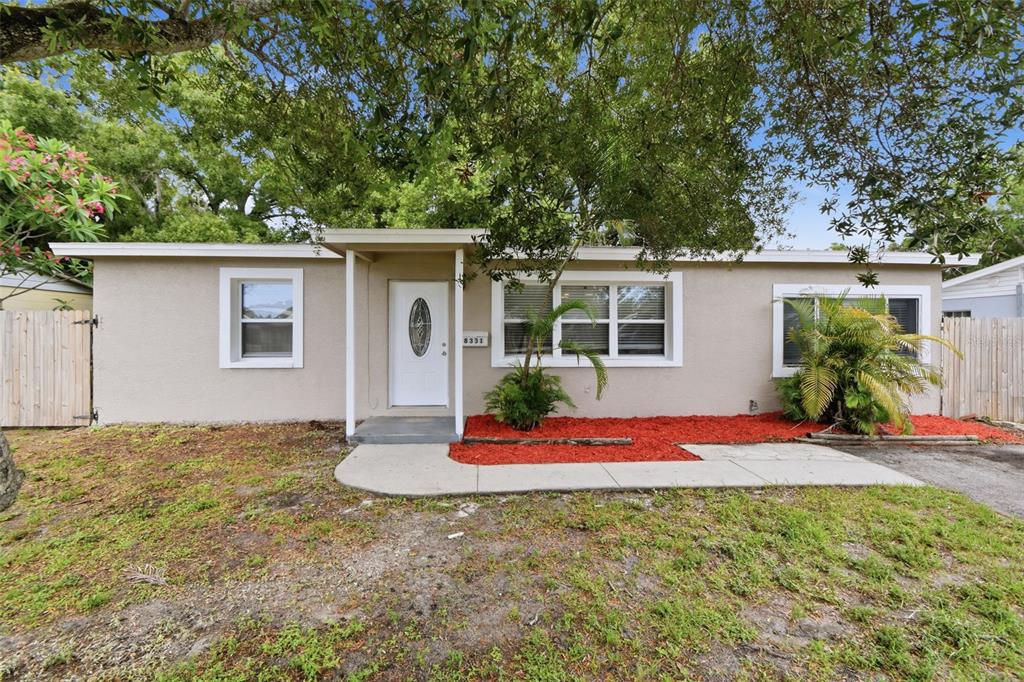 A single-story house with beige stucco siding, a white front door, and red mulch landscaping — 8331 55TH STREET N, PINELLAS PARK, FL