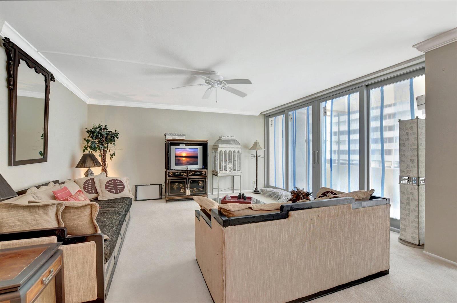 A living room features beige carpet, two sofas, a television console, and floor-to-ceiling sliding windows — 1180 S Ocean Boulevard # 2e, Boca Raton FL 33432, BOCA RATON, FL