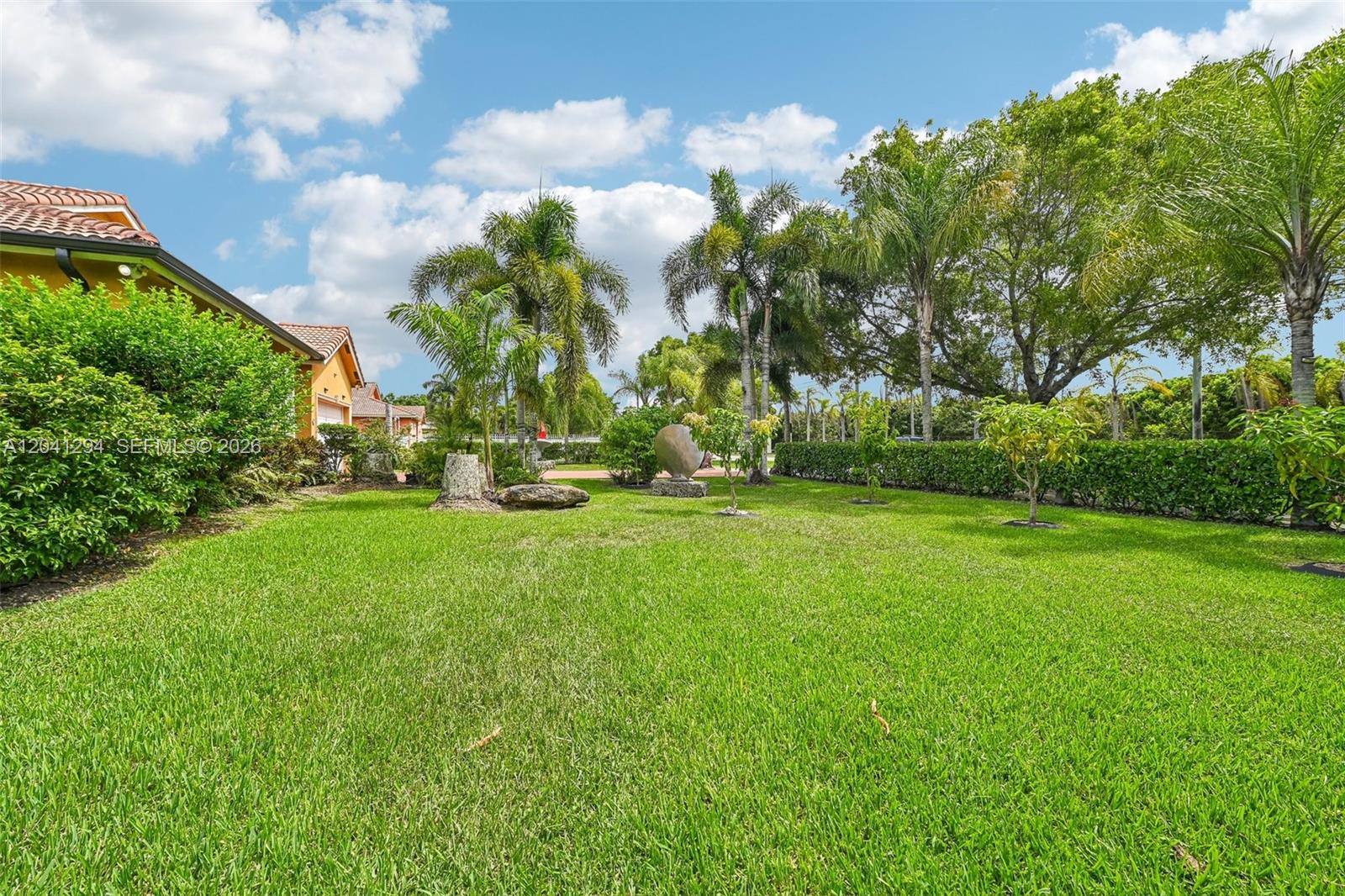 A grassy backyard features palm trees, a hedge, and a house with a tiled roof — 21401 SW 187th Ave, Miami FL 33187, MIAMI, FL
