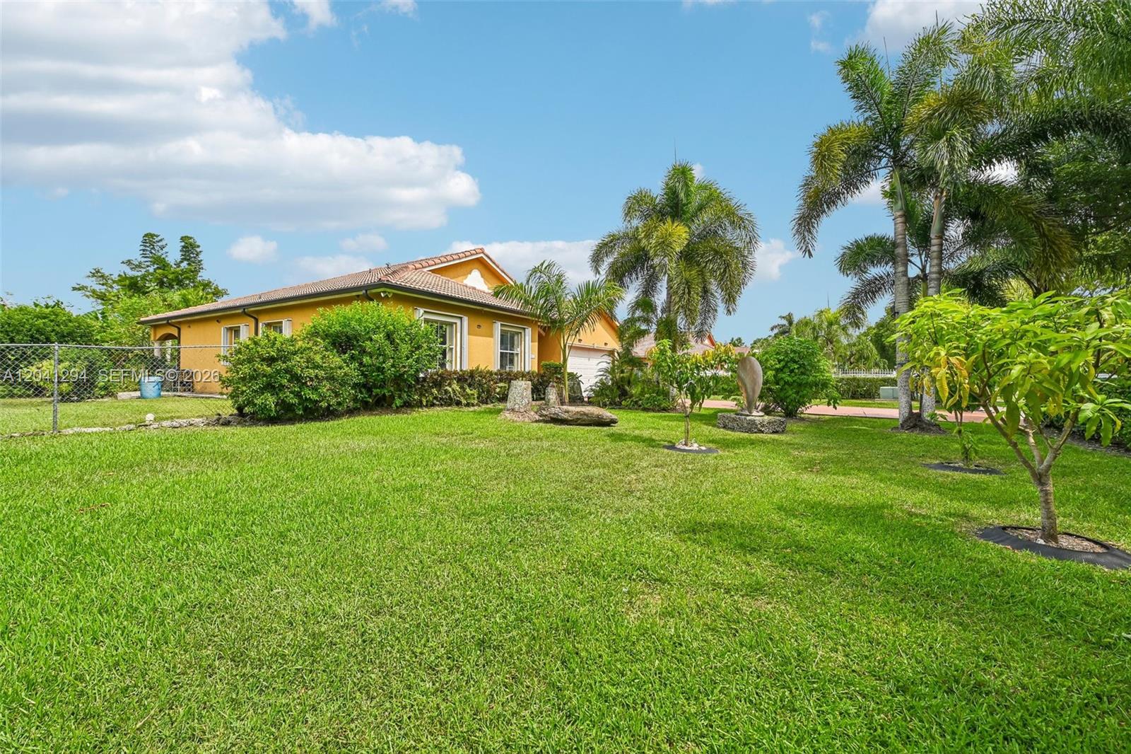 A yellow single-story house with a tile roof stands behind a large grassy lawn — 21401 SW 187th Ave, Miami FL 33187, MIAMI, FL