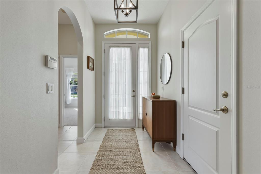 A bright entryway features tile flooring, a wooden console table, and a glass-paneled front door — 565 GREENLEAF LANE, TITUSVILLE, FL