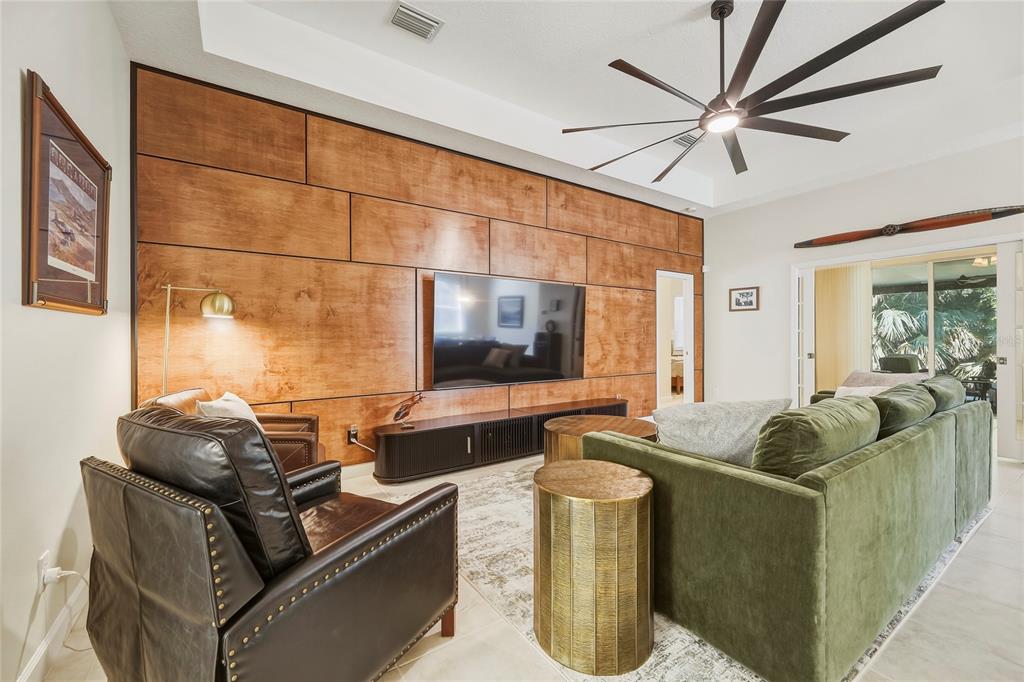 A living room features a large wood-paneled accent wall, a television, and a green sofa — 565 GREENLEAF LANE, TITUSVILLE, FL