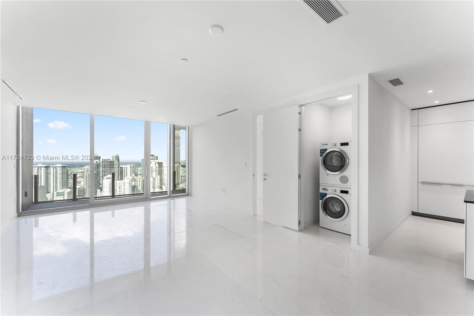 A bright, minimalist room features white tile floors, floor-to-ceiling windows, and a stacked laundry unit — 300 Biscayne Blvd Way # 5209, Miami FL 33131, MIAMI, FL