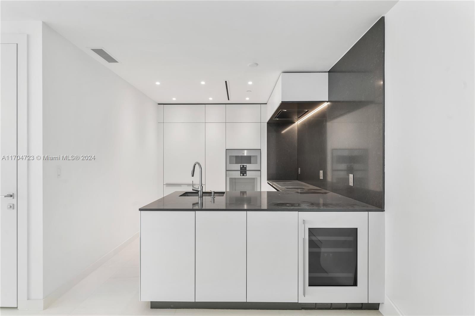 A modern kitchen features white cabinetry, a dark stone island, and a wine refrigerator — 300 Biscayne Blvd Way # 5209, Miami FL 33131, MIAMI, FL