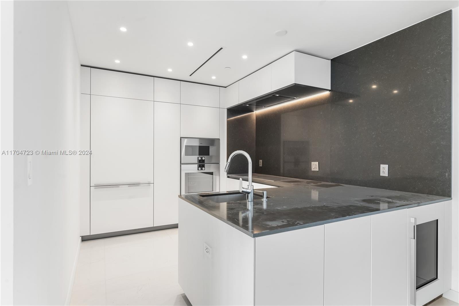 A modern kitchen features white cabinetry, a dark stone island, and a matching backsplash — 300 Biscayne Blvd Way # 5209, Miami FL 33131, MIAMI, FL