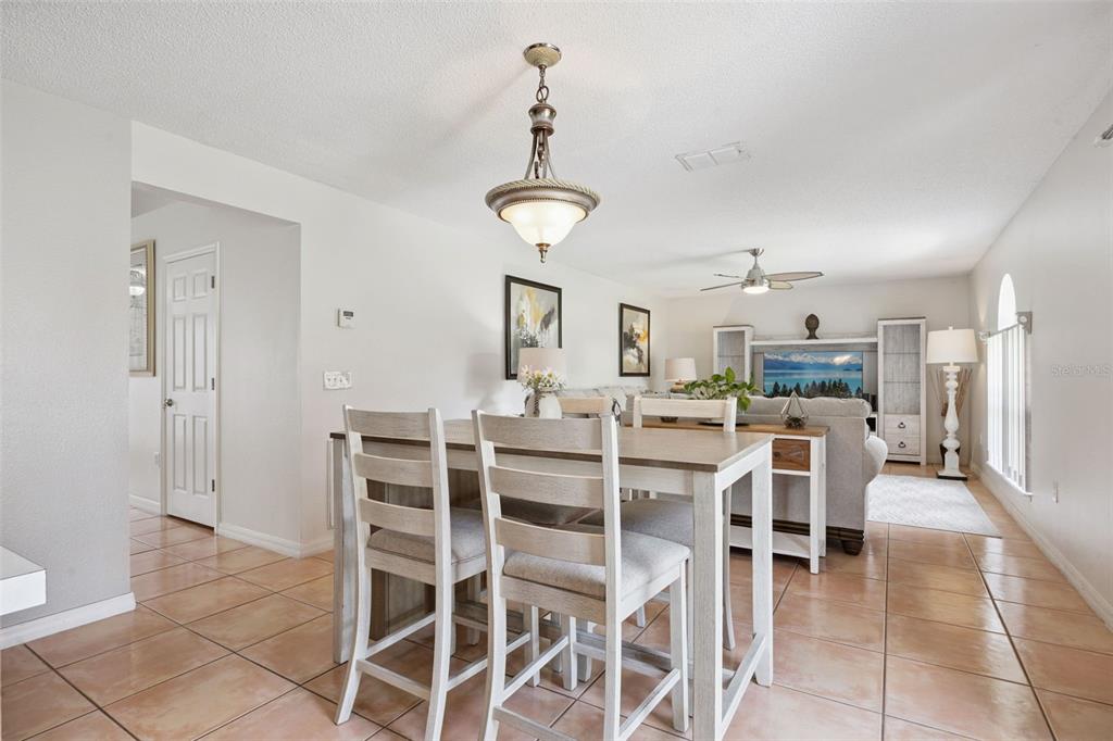 A dining area with a light wood table and chairs sits before a living room — 670 BROWN BEAR COURT, ST CLOUD, FL