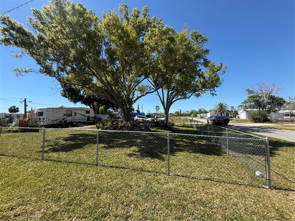 A large tree shades a grassy yard enclosed by a chain-link fence — 3830 BRAVO RD. ROAD, PORT CHARLOTTE, FL