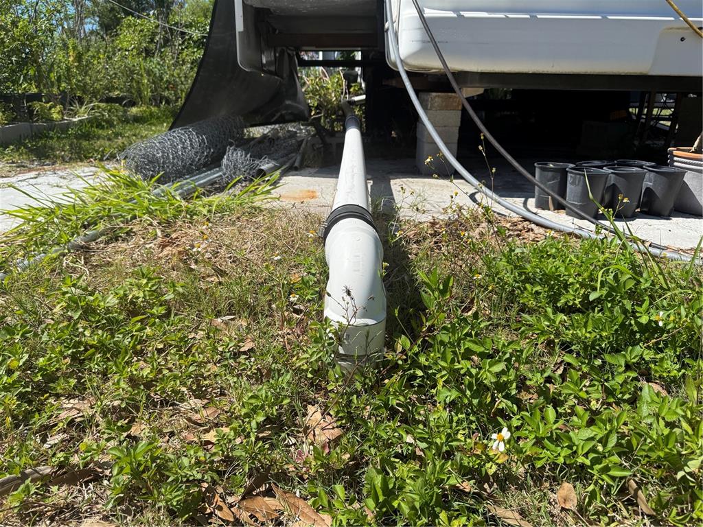 A white PVC sewer pipe connects a recreational vehicle to an underground drain in grass — 3830 BRAVO RD. ROAD, PORT CHARLOTTE, FL