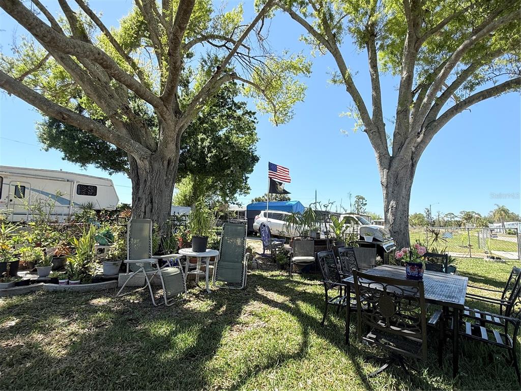 A backyard features mature trees, outdoor furniture, a dining set, and an American flag — 3830 BRAVO RD. ROAD, PORT CHARLOTTE, FL