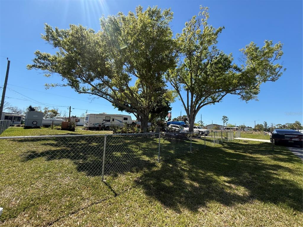 A fenced grassy yard features two large trees and a parked recreational vehicle — 3830 BRAVO RD. ROAD, PORT CHARLOTTE, FL