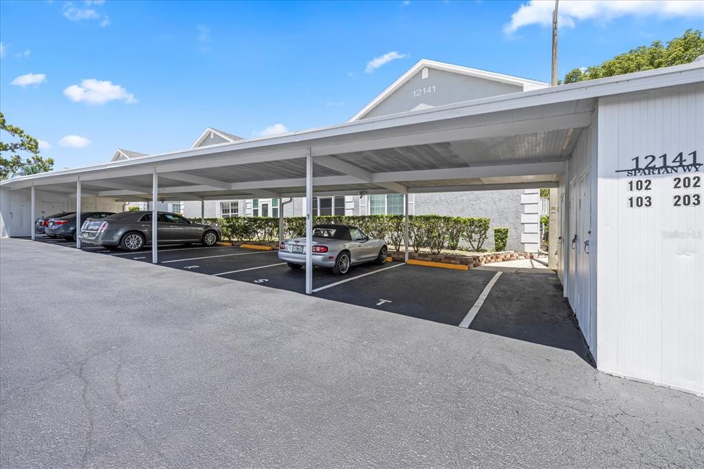 A covered parking area with several cars parked in front of a residential building — 12141 SPARTAN WAY UNIT 102, HUDSON, FL
