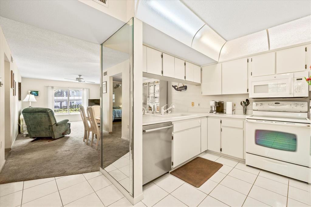 A kitchen with white cabinets and appliances features a mirrored wall and tiled flooring — 12141 SPARTAN WAY UNIT 102, HUDSON, FL
