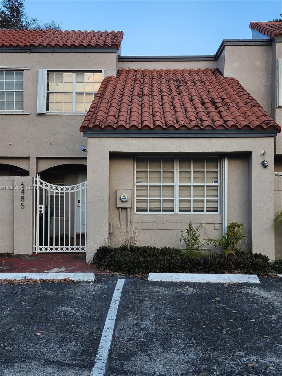 A two-story townhouse exterior features a red tile roof, white metal gate, and parking space — 6485 SW 129th Ave, Miami FL 33183, MIAMI, FL