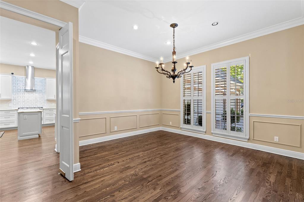 A dining room with hardwood floors, wainscoting, a chandelier, and plantation shutters on the windows — 873 CRANES COURT, MAITLAND, FL