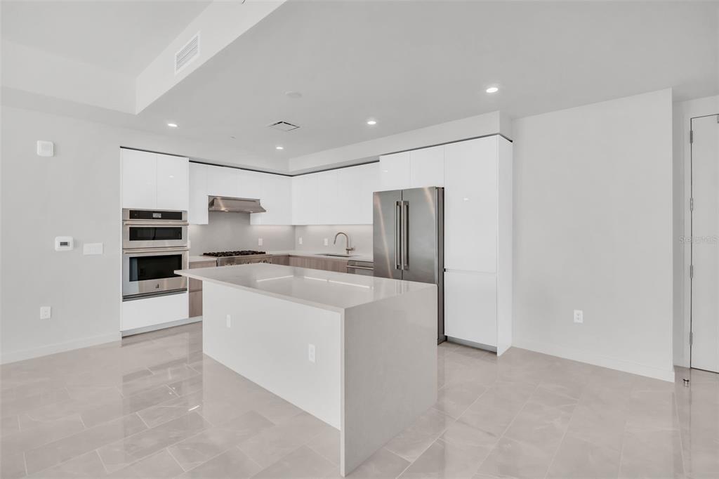 A modern kitchen features white glossy cabinets, stainless steel appliances, and a large quartz island — 400 CENTRAL AVENUE UNIT 2205, ST PETERSBURG, FL