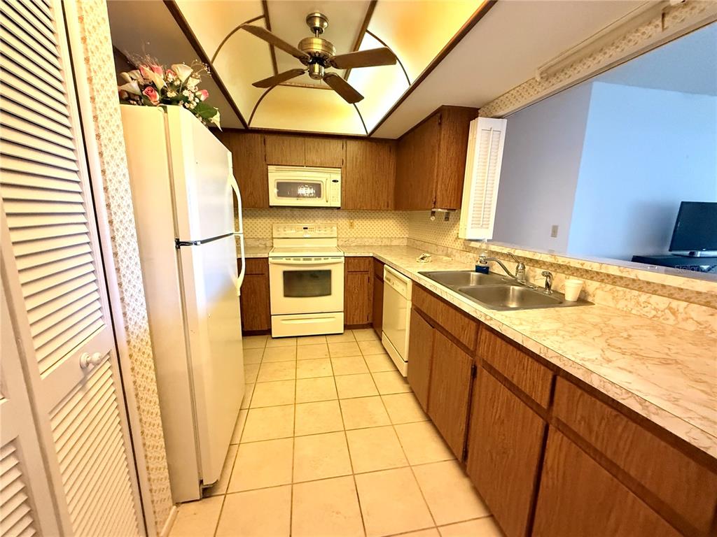 A kitchen features wood cabinets, white appliances, tile flooring, and a pass-through window — 8111 BUGLE COURT UNIT 2, PORT RICHEY, FL