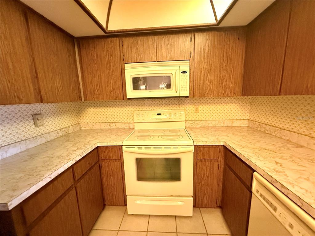 A kitchen with wood cabinets, white appliances, laminate countertops, and a tiled floor — 8111 BUGLE COURT UNIT 2, PORT RICHEY, FL