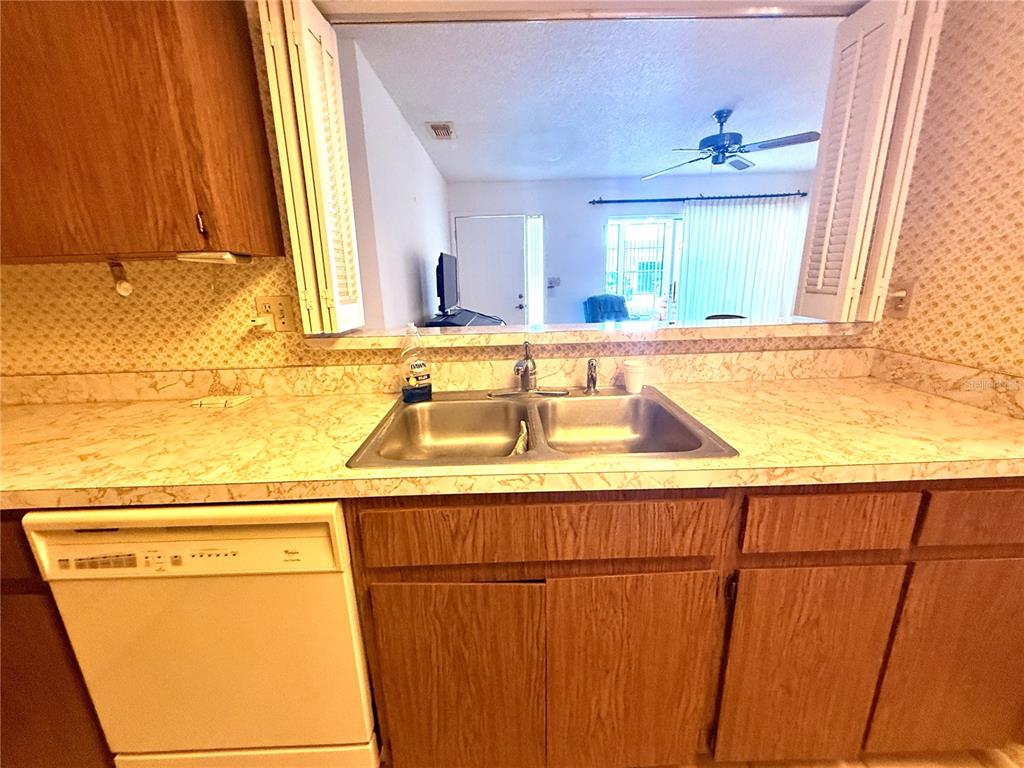 A kitchen sink and dishwasher are set against a pass-through window looking into a living area — 8111 BUGLE COURT UNIT 2, PORT RICHEY, FL