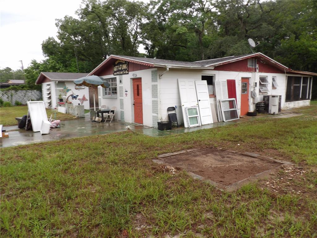A single-story white building with red doors and a small patio area sits on grass — 9706 MOON LAKE RD, NEW PORT RICHEY, FL