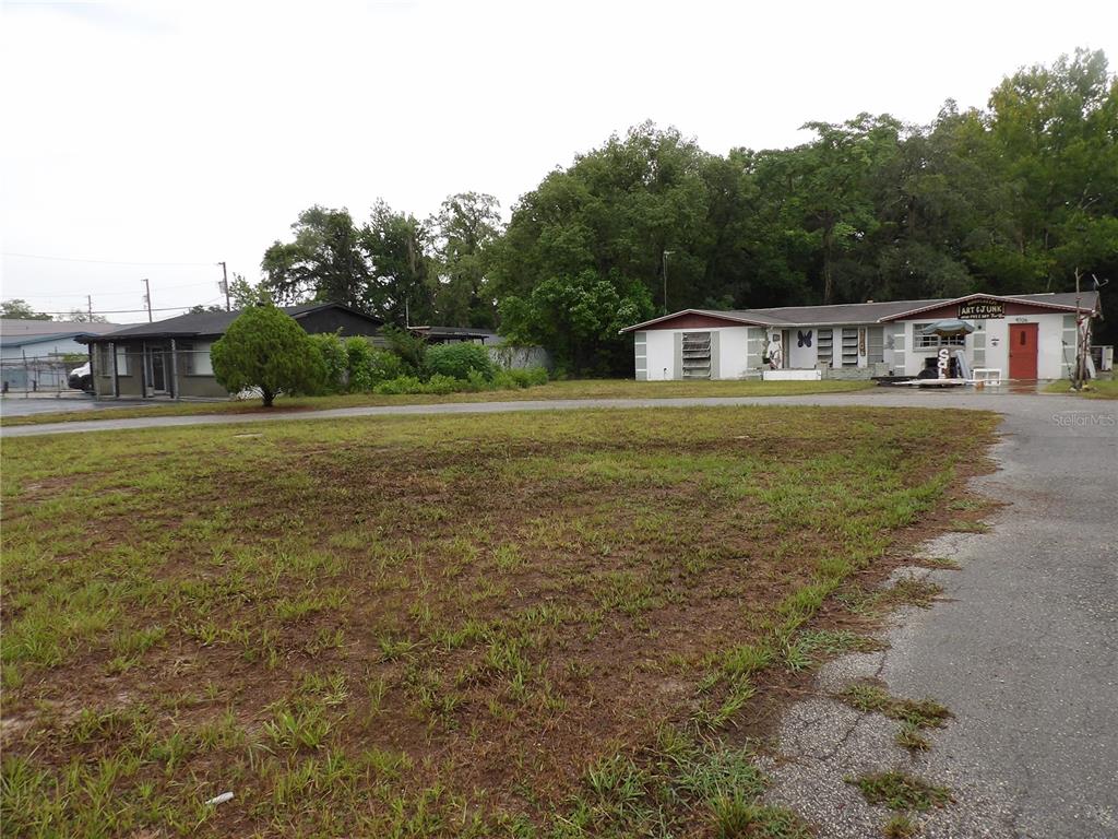 A gravel lot sits in front of two single-story buildings surrounded by trees — 9706 MOON LAKE RD, NEW PORT RICHEY, FL