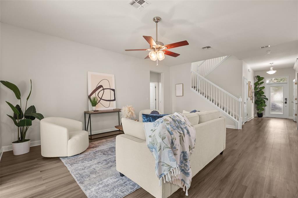 A living room features a sofa, accent chair, area rug, and staircase with white railings — 34004 ALAMEDA DRIVE, SORRENTO, FL