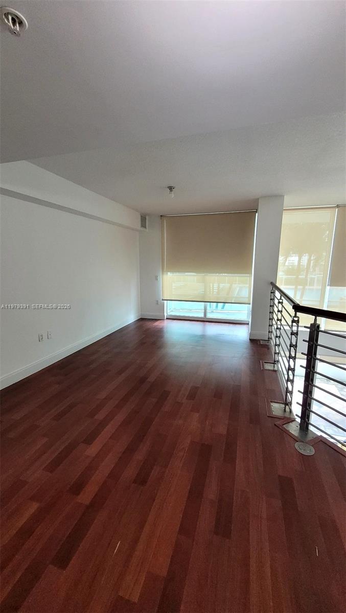 An empty room features dark wood flooring, white walls, and a metal staircase railing — 41 SE 5th St # 709, Miami FL 33131, MIAMI, FL