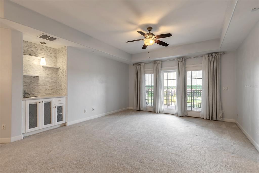 A carpeted room features a wet bar with tile backsplash and glass doors to a balcony — 424 LUNA BELLA LANE UNIT 415, NEW SMYRNA BEACH, FL