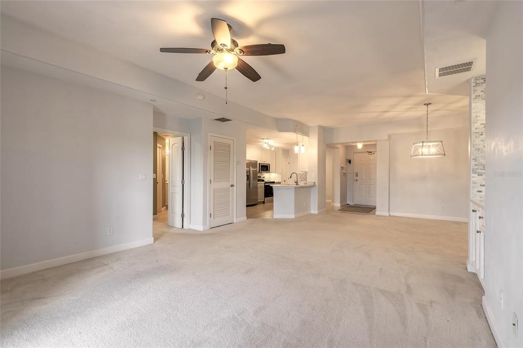 A spacious living area with beige carpeting, a ceiling fan, and an open-concept kitchen — 424 LUNA BELLA LANE UNIT 415, NEW SMYRNA BEACH, FL