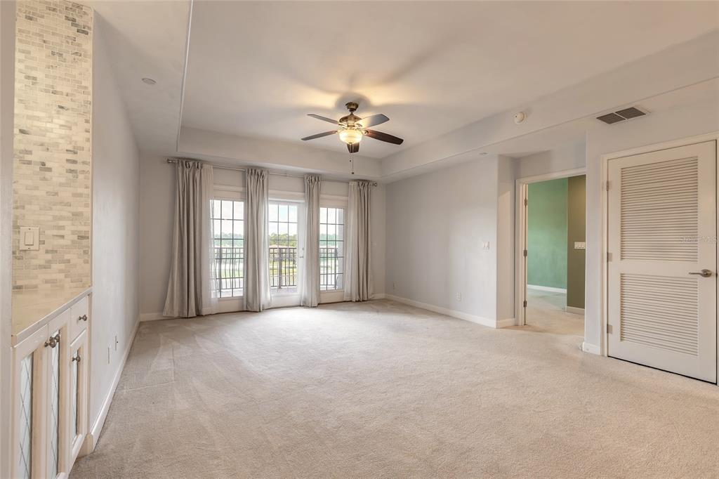 A carpeted bedroom features a tray ceiling, a ceiling fan, and glass doors to a balcony — 424 LUNA BELLA LANE UNIT 415, NEW SMYRNA BEACH, FL