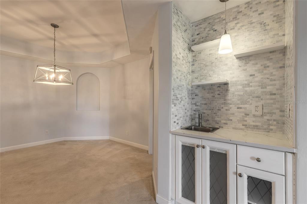 A wet bar with white cabinets and tiled backsplash sits beside a carpeted dining area — 424 LUNA BELLA LANE UNIT 415, NEW SMYRNA BEACH, FL